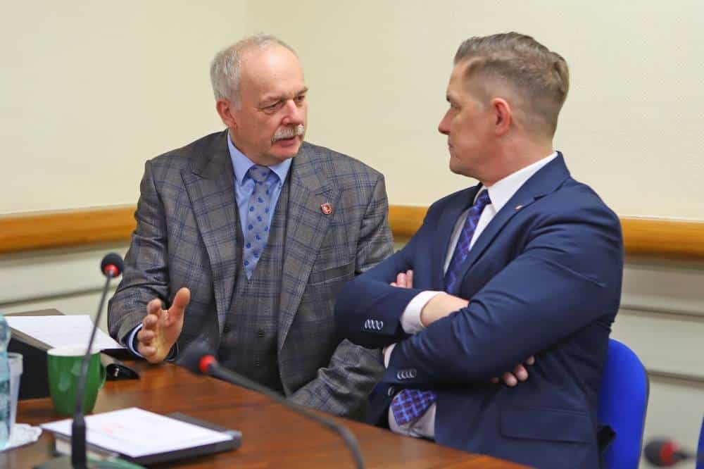 Dwaj mężczyźni w formalnych strojach prowadzą rozmowę w trakcie sesji rady powiatu.