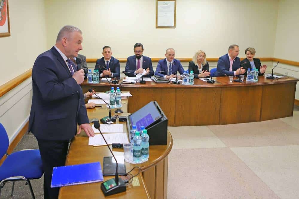 Na zdjęciu widoczna jest sesja rady powiatu, podczas której przewodniczący wygłasza przemówienie, a pozostali członkowie rady słuchają i uczestniczą w dyskusji.