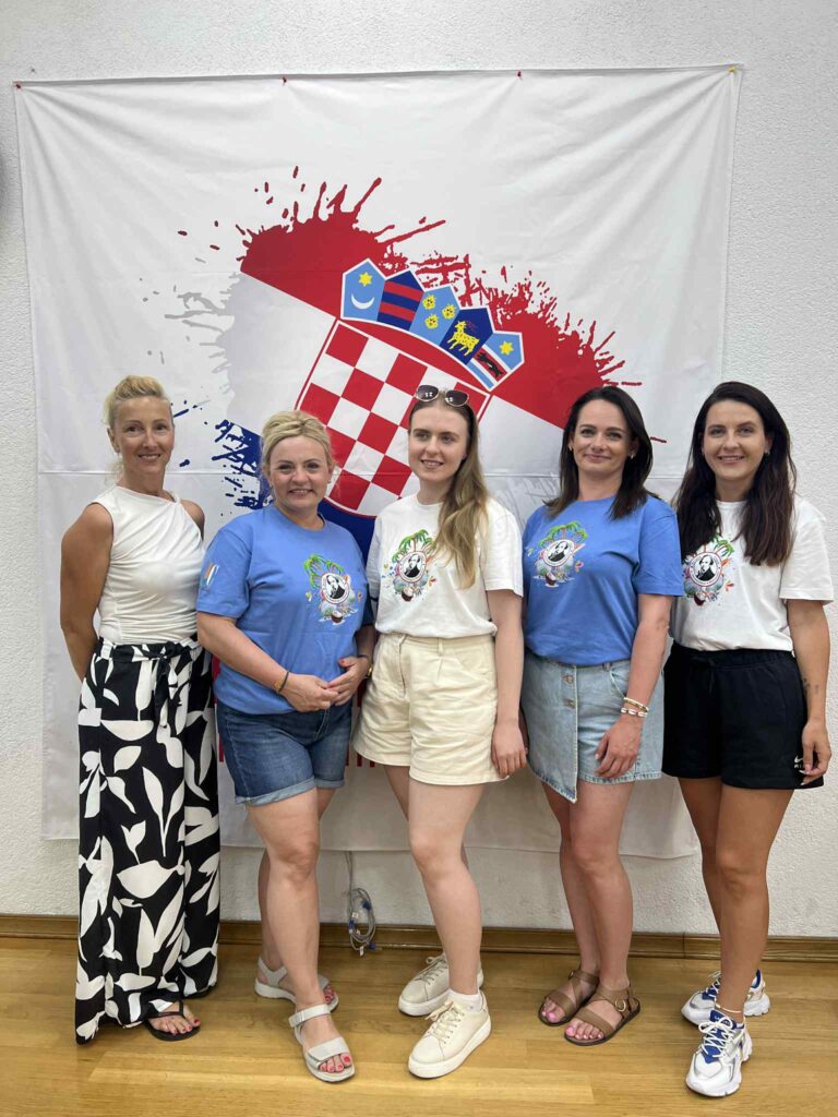 Na zdjęciu widać pięć kobiet stojących przed flagą z motywami chorwackimi, uśmiechających się podczas wyjazdu młodzieży i kadry ZS im. Jana Śniadeckiego w Wyszogrodzie.
