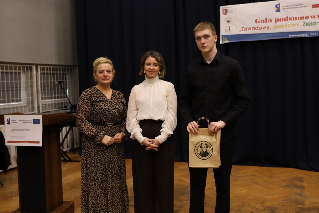 Na zdjęciu widoczni są trzej uczestnicy gali podsumowującej projekt FERS, prezentujący się w eleganckich strojach, przy stole z logo Unii Europejskiej oraz transparentem projektu.