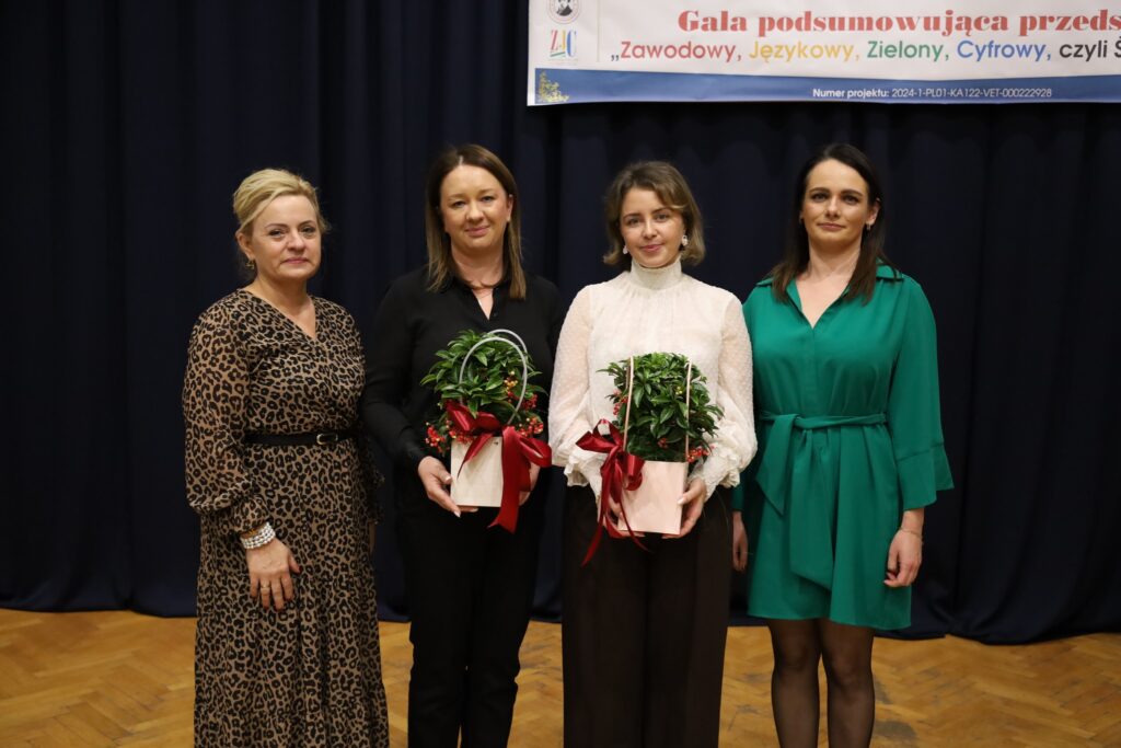 Na zdjęciu cztery kobiety stojące obok siebie, trzymające doniczki z roślinami, podczas gali podsumowującej przedsięwzięcie FERS „Zawodowy, Językowy, Zielony, Cyfrowy, czyli Śniadecki na Stażu”.