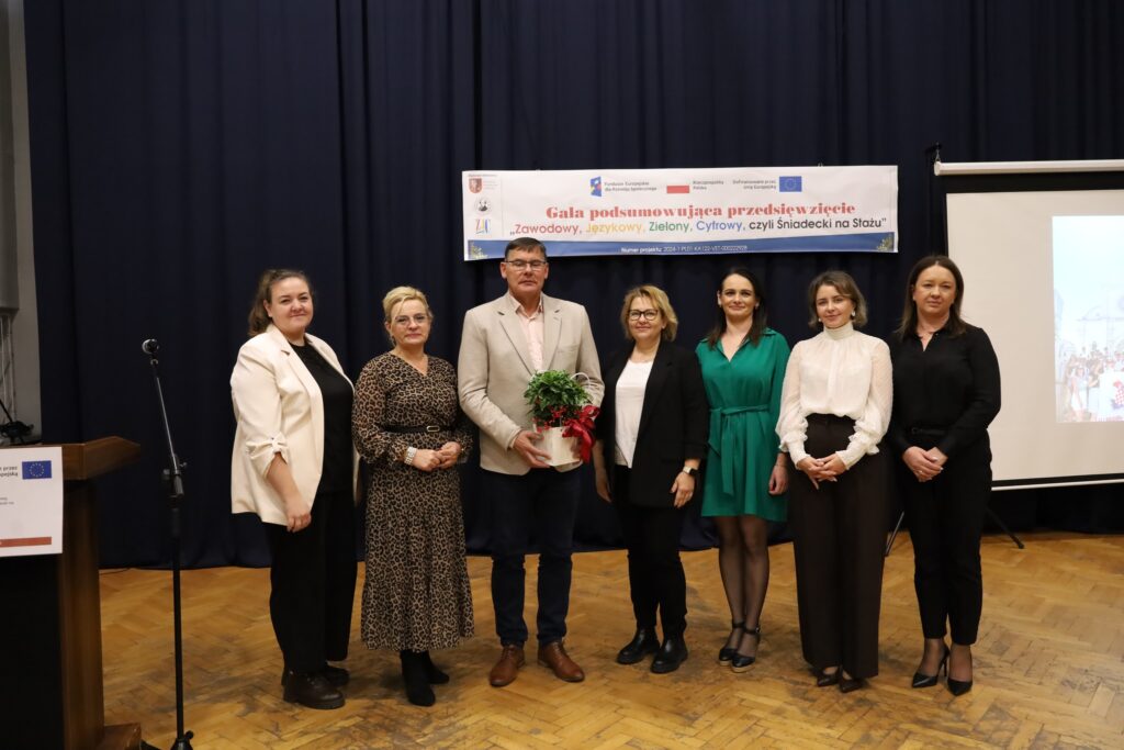 Gala podsumowująca przedsięwzięcie FERS „Zawodowy, Językowy, Zielony, Cyfrowy, czyli Śniadecki na Stażu” z uczestnikami i organizatorami, trzymającymi roślinę jako symbol współpracy.
