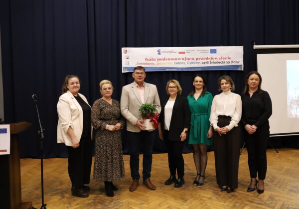 Gala podsumowująca przedsięwzięcie FERS „Zawodowy, Językowy, Zielony, Cyfrowy, czyli Śniadecki na Stażu” z uczestnikami i organizatorami, trzymającymi roślinę jako symbol współpracy.