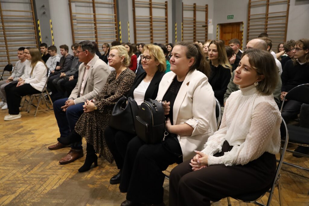 Uczestnicy gali podsumowującej projekt FERS siedzą w sali, wyrażając zainteresowanie podczas wydarzenia.