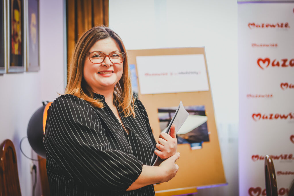 Młodzieżowa radna uśmiecha się, trzymając w ręku dokumenty podczas ceremonii wręczenia nagród laureatom konkursu.