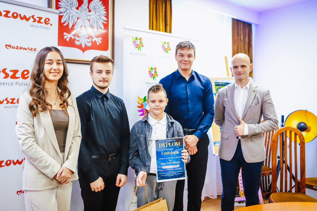 Młodzieżowi Radni Powiatu Płockiego wręczają nagrody laureatom konkursu w przyjaznej atmosferze, prezentując dyplomy i uśmiechy.