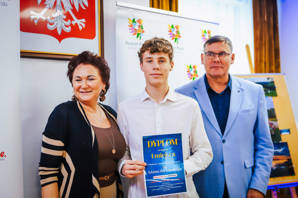 Młodzieżowi Radni Powiatu Płockiego wręczają dyplom laureatowi konkursu, na którym widać uśmiechniętą grupę osób.