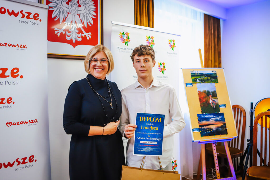 Na zdjęciu widać uśmiechniętą kobieta i młodego mężczyznę, trzymających dyplom za pierwsze miejsce w konkursie, podczas wydarzenia organizowanego przez Młodzieżowych Radnych Powiatu Płockiego.