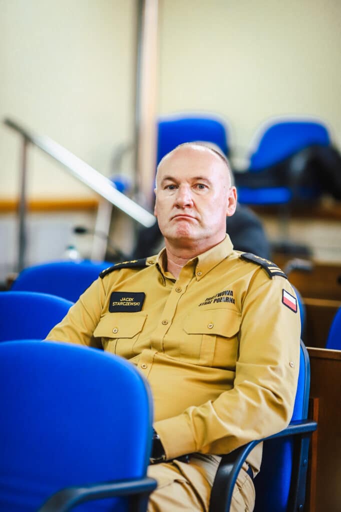 Na zdjęciu widać mężczyznę w mundurze strażackim, który siedzi na sali obrad podczas XVI Sesji Rady Powiatu w Płocku.