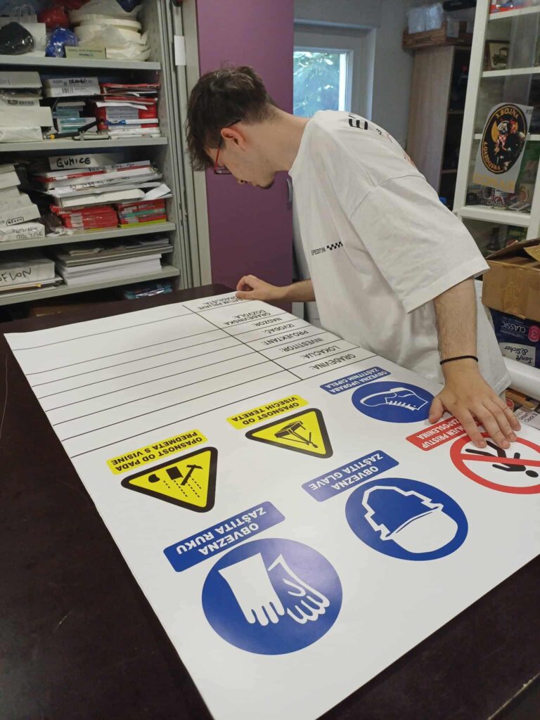 Młody mężczyzna pracuje nad odznakami z instrukcjami bezpieczeństwa, przygotowując materiał edukacyjny w ramach projektu FERS.