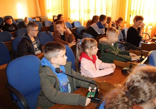 Zdjęcie przedstawia grupę dzieci z podstawówki, które uczestniczą w wizytacji w sali obrad starostwa powiatowego w Płocku.