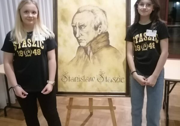Na zdjęciu dwie młode kobiety stoją obok portretu Stanisława Staszica.