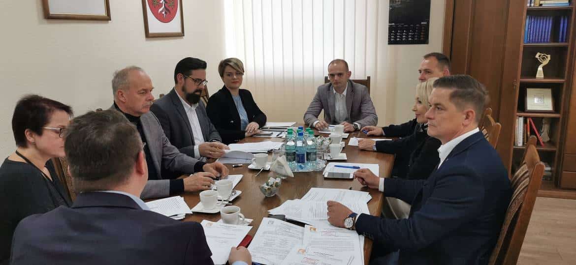 Zdjęcie przedstawia grupę osób siedzących przy stole podczas spotkania roboczego, otoczoną dokumentami i filiżankami z kawą.