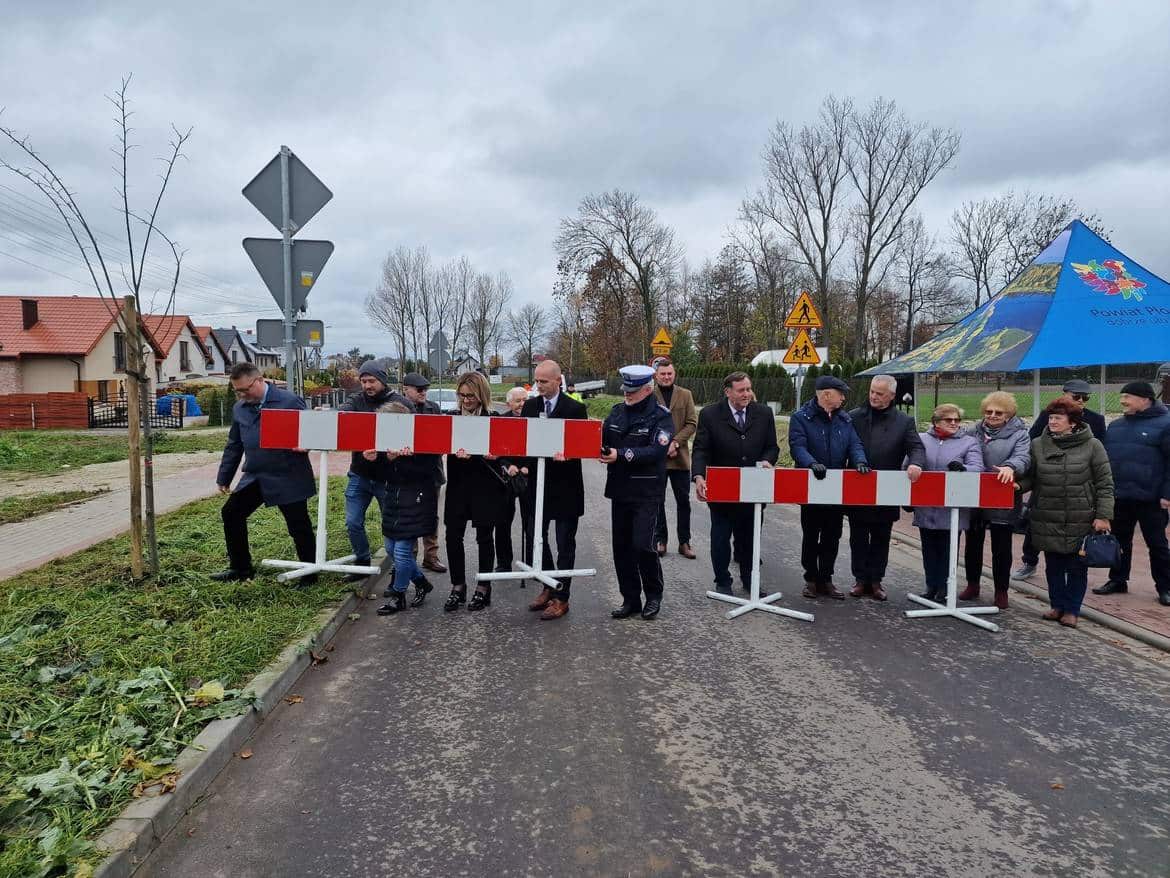 Na zdjęciu widać grupę osób, w tym przedstawicieli władz, trzymających barierki drogowe podczas formalnej ceremonii otwarcia lub zakończenia prac na drodze.