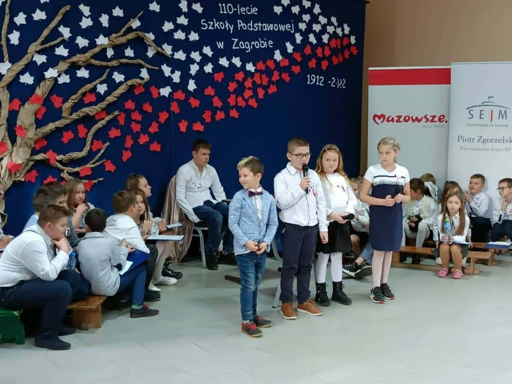 Dzieci w strojach galowych przemawiają podczas uroczystości z okazji 110-lecia Szkoły Podstawowej w Zagrobie.