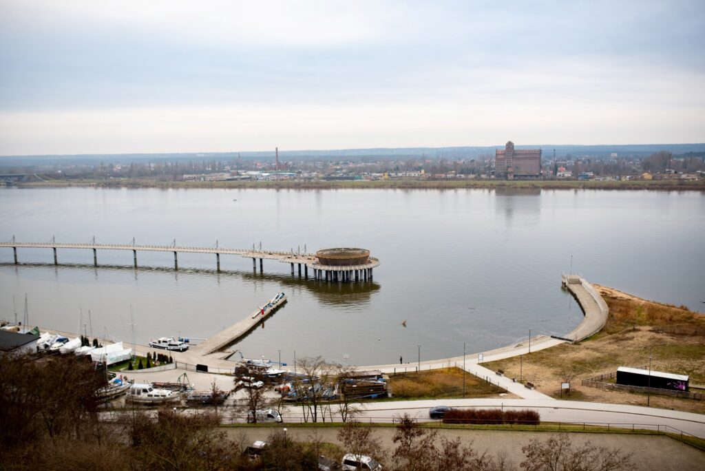 Widok na rzekę z nowo wybudowanym pomostem oraz przystanią w Płocku, podkreślający działania na rzecz poprawy bezpieczeństwa powodziowego.