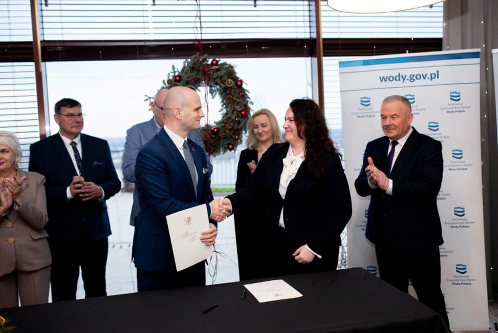 Na zdjęciu przedstawiono uroczystość podpisania umowy dotyczącej przywracania bezpieczeństwa powodziowego, z udziałem Starosty Płockiego oraz innych przedstawicieli, którzy wyrazili radość z tego wydarzenia.