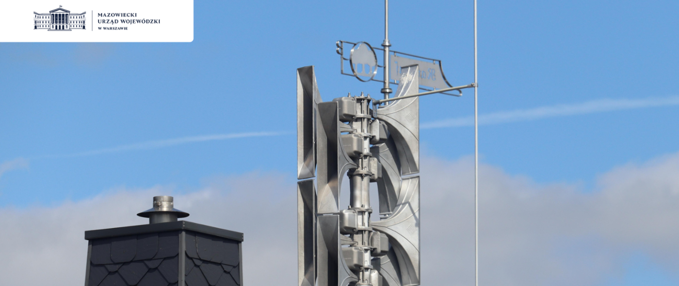 Na zdjęciu znajduje się głośnik systemu alarmowego, umieszczony na dachu budynku, w tle błękitne niebo z chmurami.