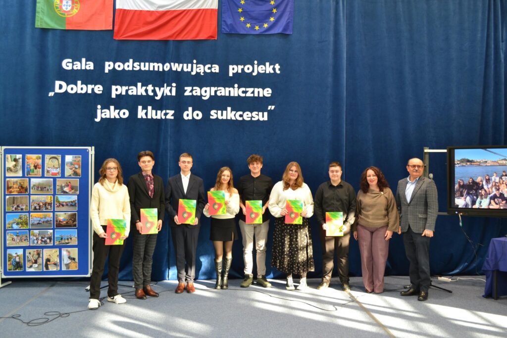 Uczestnicy gali podsumowującej projekt „Dobre praktyki zagraniczne jako klucz do sukcesu” pozują z certyfikatami, a w tle widoczne są flagi oraz plansza z fotografiami.