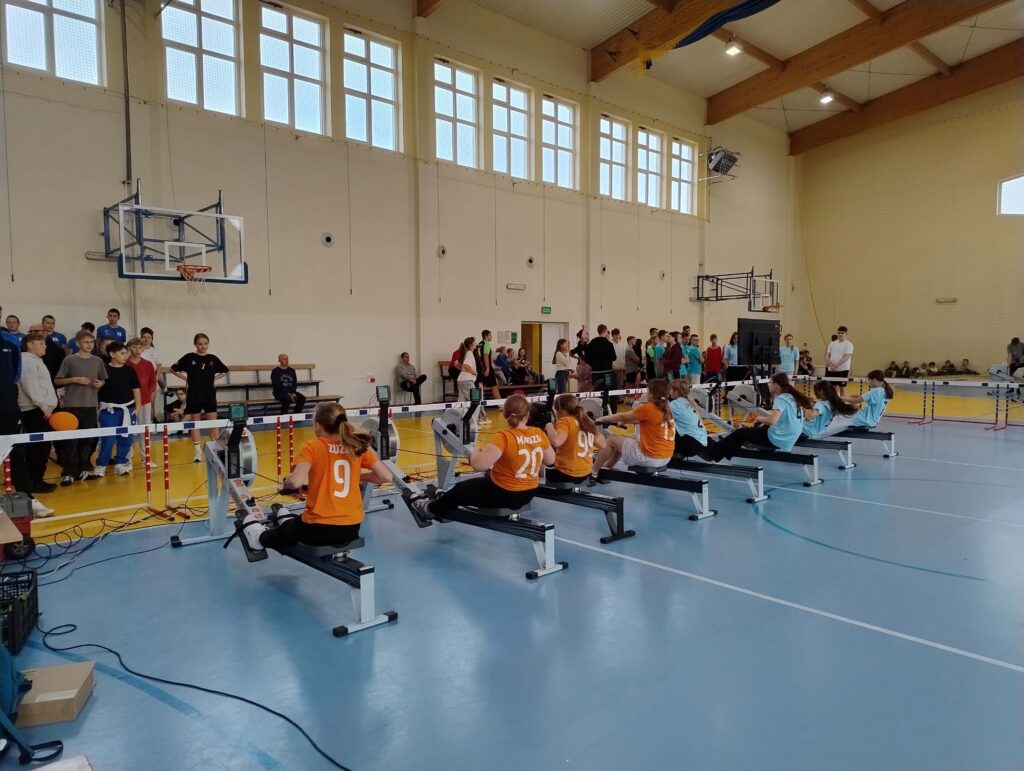 Finał powiatowy w ergowioślarstwie w 2025 roku, z zawodnikami rywalizującymi na wioślarzach w sportowej hali.
