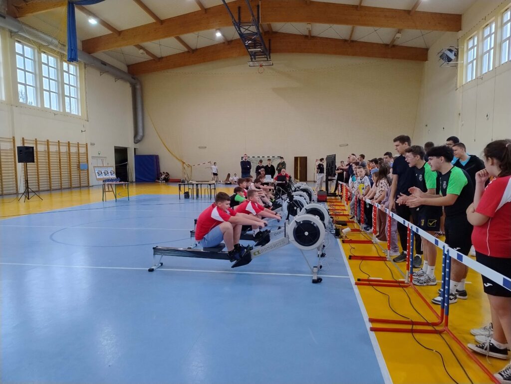 Na zdjęciu widać uczestników finału powiatowego zawodów ergowiosłowych, którzy rywalizują na ergometrach w obecności licznej publiczności.