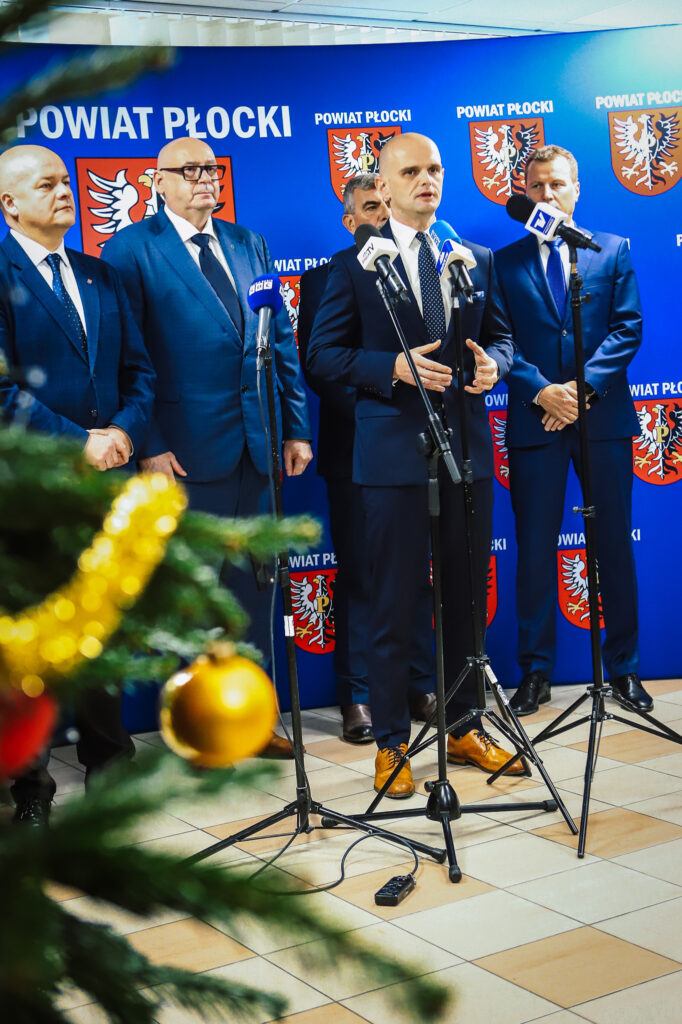 Konferencja prasowa z podpisania aktu notarialnego dotyczącego rozwoju wojskowości w powiecie płockim, z przedstawicielami władz lokalnych w tle.