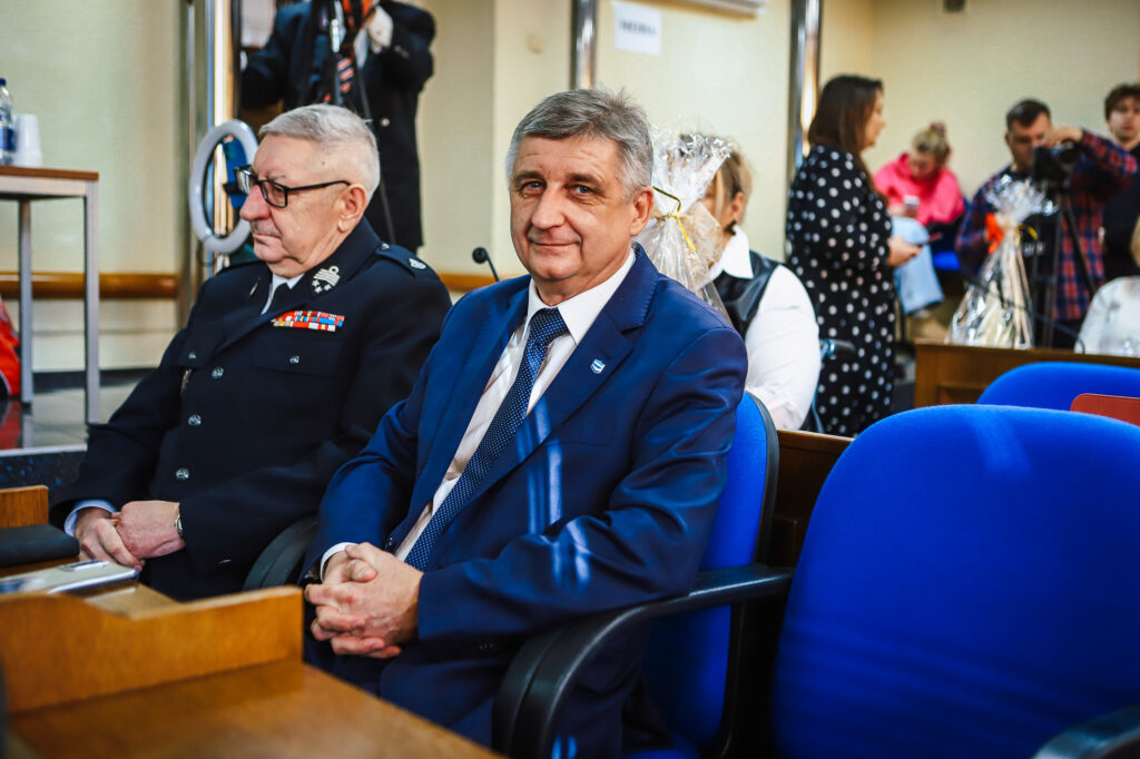 Radni Powiatu Płockiego uczestniczą w sesji, podczas której uchwalany jest rekordowy budżet, a w tle widać zebranych gości.