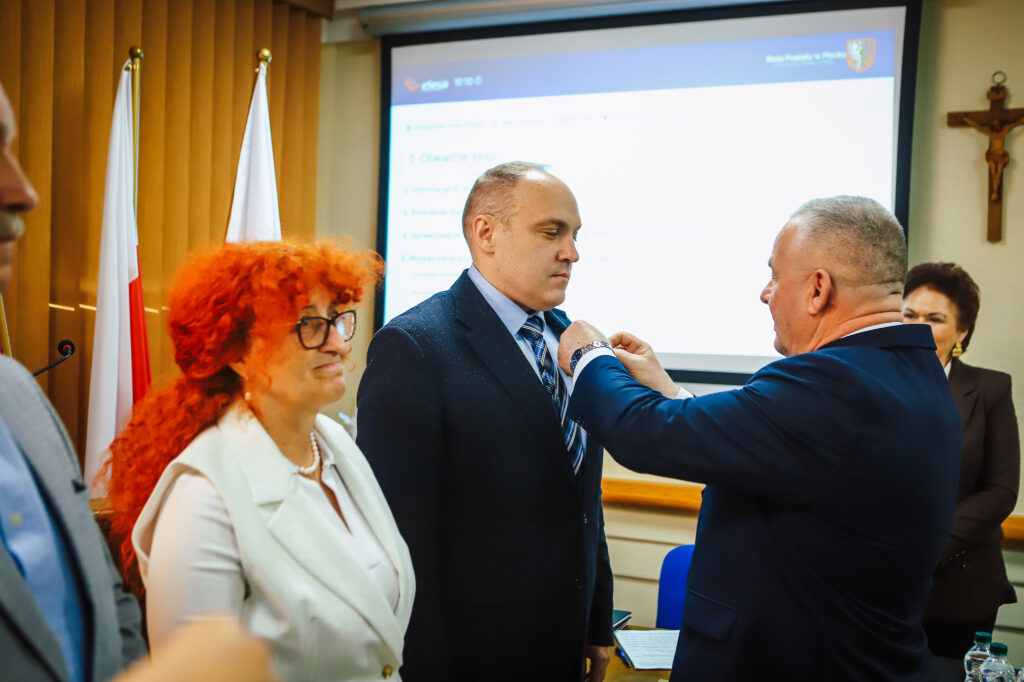 Na zdjęciu radni Powiatu Płockiego uczestniczą w ceremonii uchwalenia rekordowego budżetu, w której jeden z nich jest dekorowany przez kolegę.