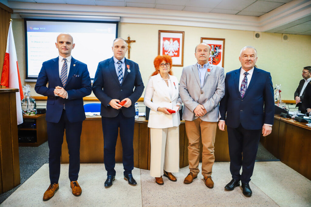 Radni Powiatu Płockiego stoją w sali obrad, trzymając pamiątkowe medale, po uchwaleniu rekordowego budżetu.