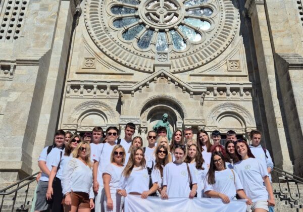 Uczestnicy projektu „Dobre praktyki zagraniczne jako klucz do sukcesu” pozują na schodach przed imponującą budowlą, trzymając flagę Polski.