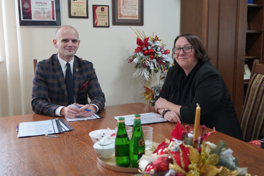 Na zdjęciu widać dwóch urzędników siedzących przy stole, otoczonych dokumentami i świątecznymi dekoracjami, co sugeruje atmosferę pracy w okresie przedświątecznym.