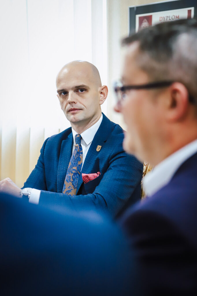 Na zdjęciu widoczny jest mężczyzna w garniturze, który słucha uważnie podczas spotkania w pomieszczeniu biurowym.