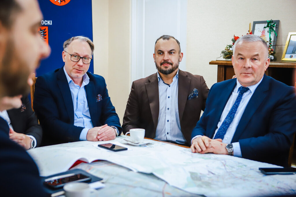 Czterech mężczyzn w garniturach siedzi przy stole z mapą, omawiając szczegóły dotyczące trasy S10 w pobliżu Płocka.