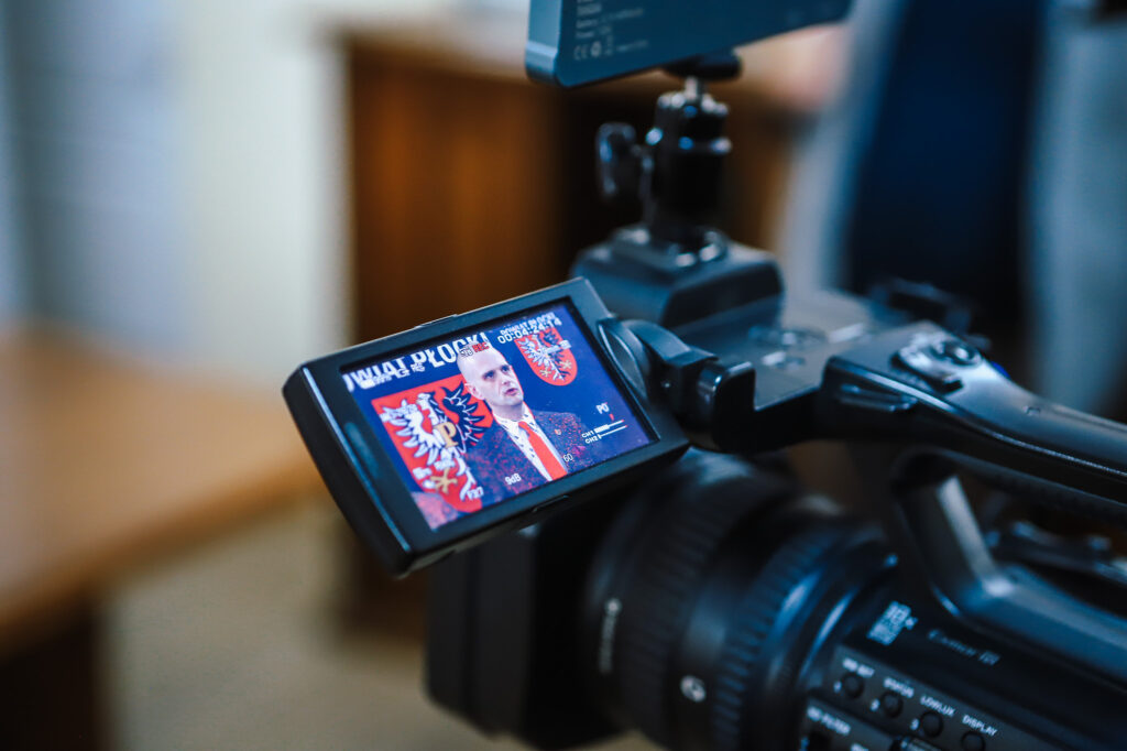 Na zdjęciu widać kamerę rejestrującą mężczyznę w garniturze, który mówi, podczas konferencji dotyczącej nowej ścieżki rowerowej w Powiecie Płockim.