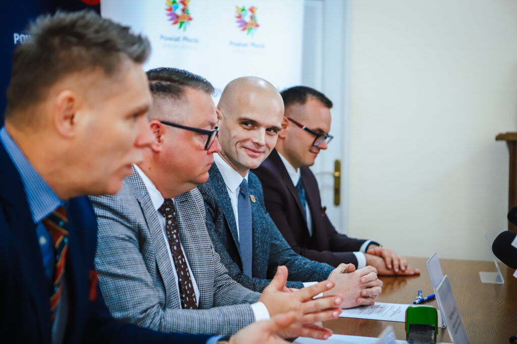 Na zdjęciu widać grupę mężczyzn w garniturach siedzących przy stole podczas spotkania dotyczącego budowy nowej ścieżki rowerowej w powiecie płockim.