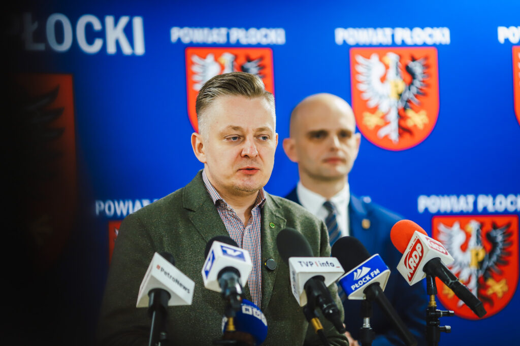 Wiceminister z Powiatu Płockiego podczas konferencji prasowej, omawia kwestie bezpieczeństwa i współpracy rządu z samorządem.