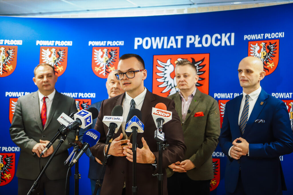 Wiceminister, otoczony przez przedstawicieli samorządu, omawia kwestie bezpieczeństwa i współpracy rządu z lokalnymi władzami podczas konferencji prasowej w Powiecie Płockim.