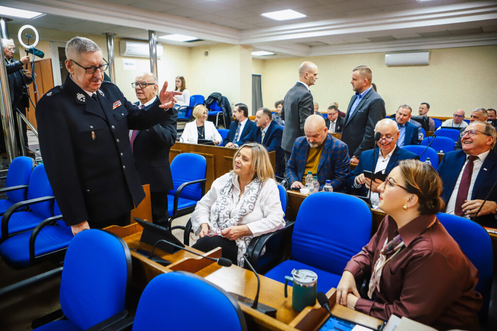 Uczestnicy XVIII Sesji Rady Powiatu w Płocku dyskutują w sali obrad, podejmując ważne decyzje dotyczące wsparcia społecznego.