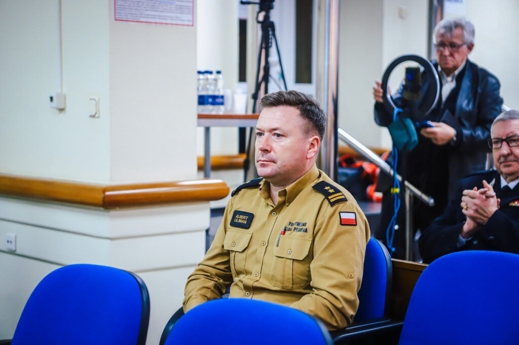 Na zdjęciu widoczny jest mężczyzna w mundurze, uczestniczący w XVIII Sesji Rady Powiatu w Płocku, skoncentrowany na dyskusji.