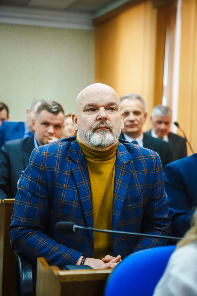 Na zdjęciu przedstawiony jest mężczyzna w eleganckim garniturze, który uczestniczy w XVIII Sesji Rady Powiatu w Płocku, gdzie omawiane są ważne społecznie decyzje.