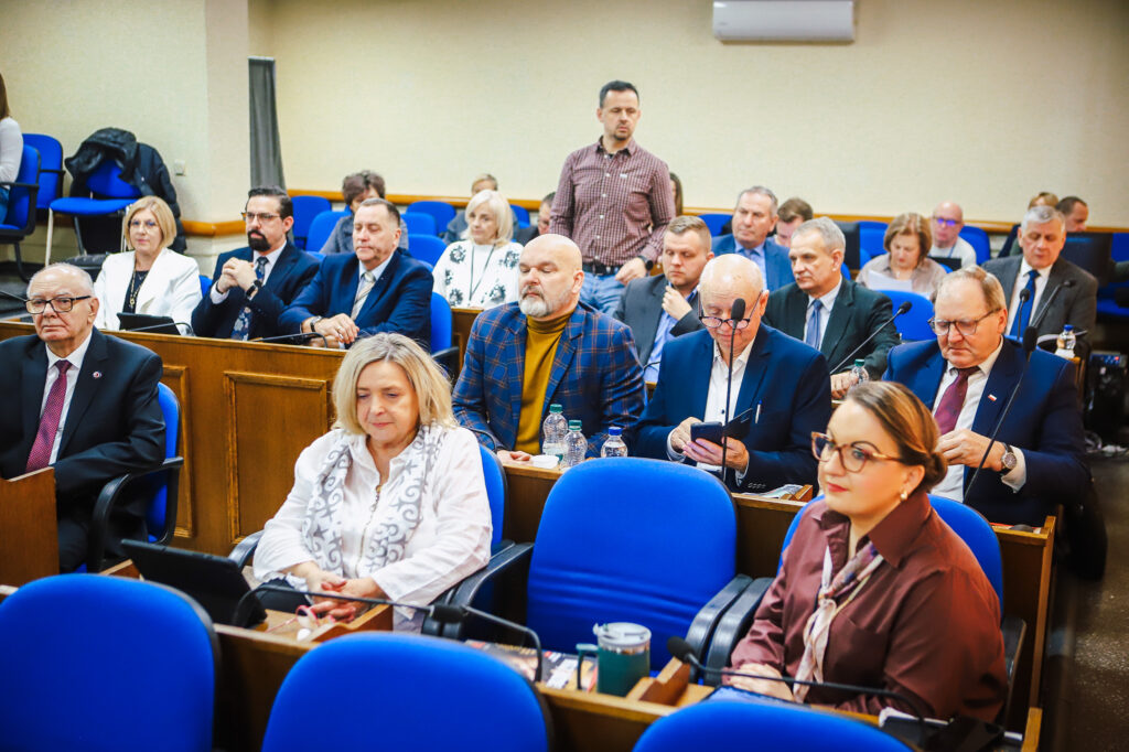Uczestnicy XVIII Sesji Rady Powiatu w Płocku, siedzący w sali obrad, biorą udział w dyskusji dotyczącej ważnych decyzji społecznych.