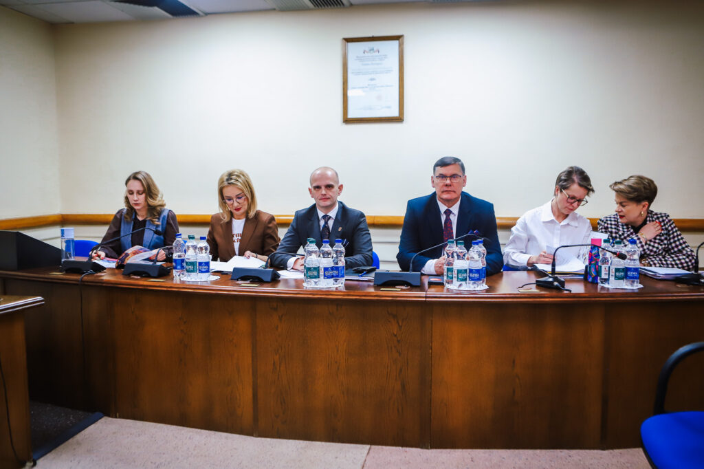 Na zdjęciu uczestnicy XVIII Sesji Rady Powiatu w Płocku siedzą przy stole, omawiając важne tematy związane z jednomyślnymi decyzjami i wsparciem społecznym.