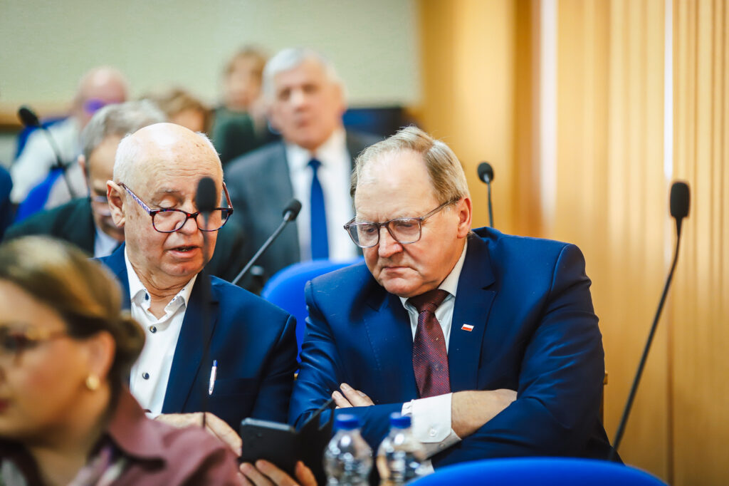 Dwóch mężczyzn w garniturach rozmawia w trakcie XVIII Sesji Rady Powiatu w Płocku.