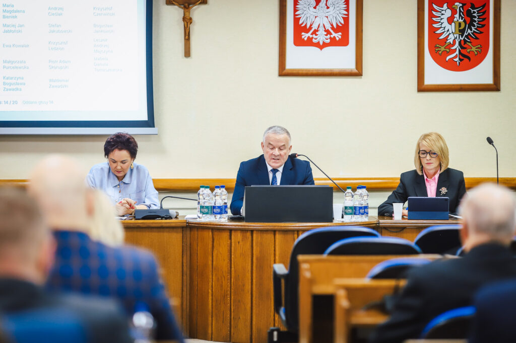 Na zdjęciu widać trzech członków Rady Powiatu w Płocku podczas XVIII Sesji, omawiających ważne decyzje dotyczące wsparcia społecznego.
