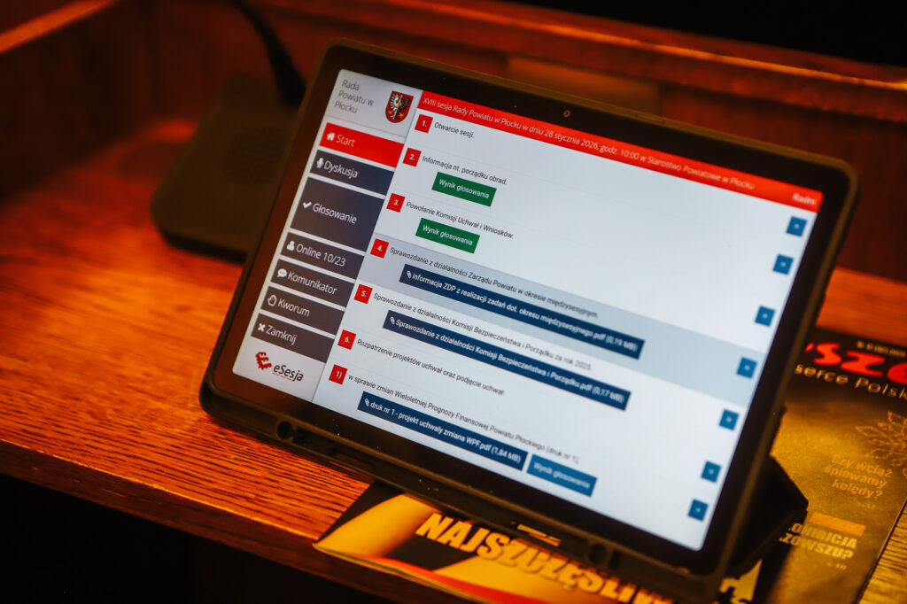 Tablet z interfejsem do głosowania i dyskusji podczas XVIII Sesji Rady Powiatu w Płocku, na którym wyświetlane są istotne tematy porządkowe.