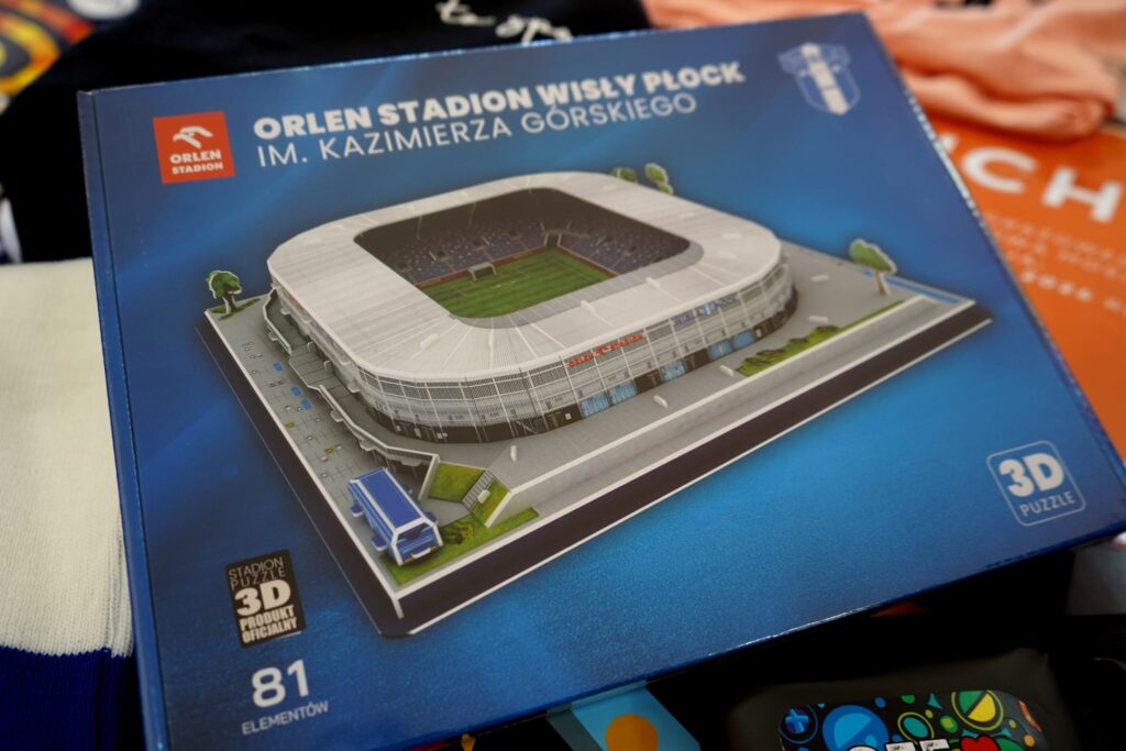 Na zdjęciu znajduje się pudełko 3D puzzli przedstawiających Orlen Stadion Wisły Płock im. Kazimierza Górskiego, z widokiem na jego bryłę i boisko.