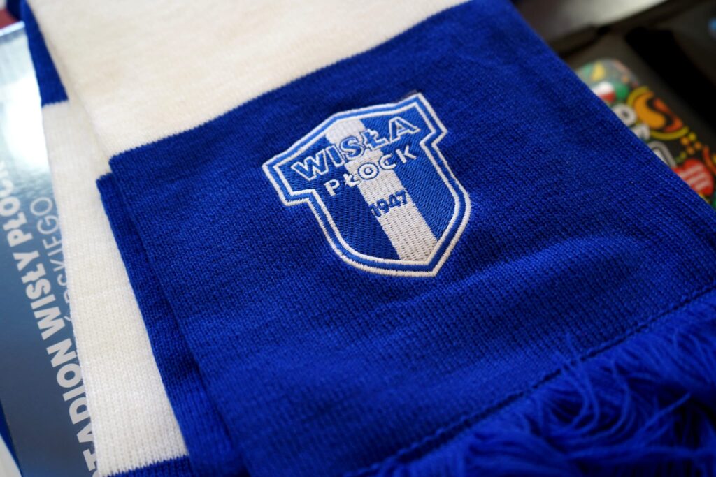 Na zdjęciu widoczny jest szalik w barwach niebiesko-białych z logo klubu sportowego Wisła Płock oraz rokiem 1947.