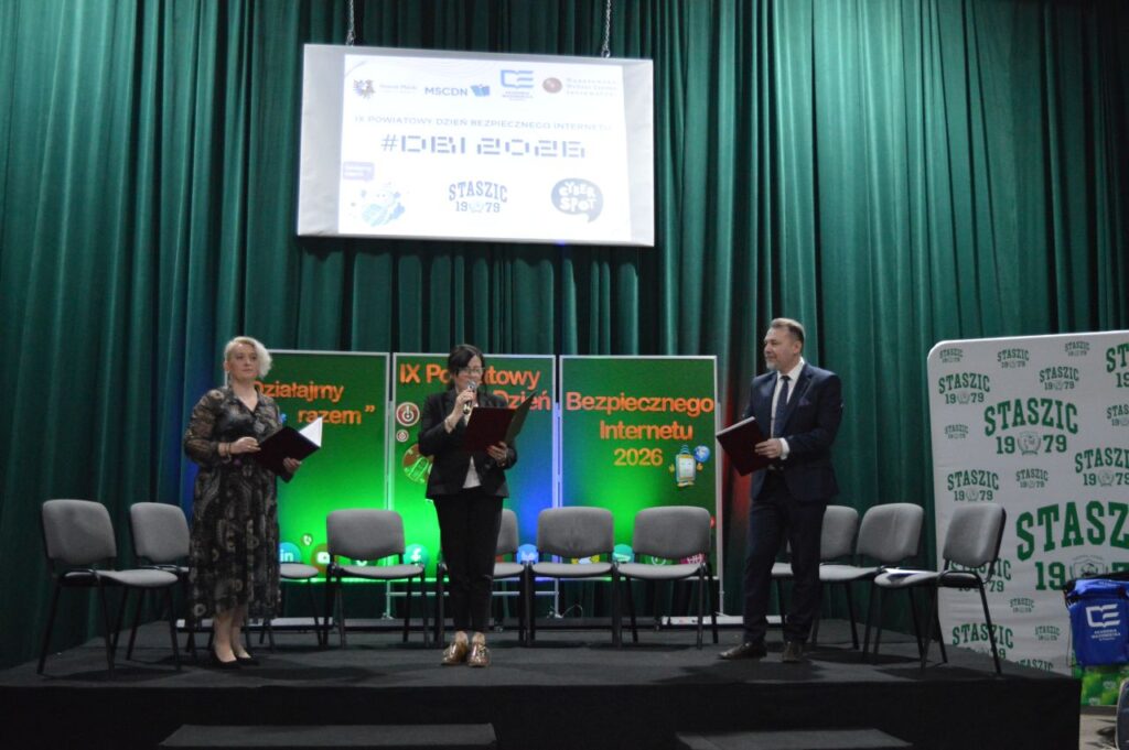 Na scenie w Zespole Szkół im. Stanisława Staszica w Gąbinie trzy osoby wygłaszają przemówienie podczas IX Powiatowego Dnia Bezpiecznego Internetu 2026, a w tle stoją zielone ścianki i baner z logotypami wydarzenia.