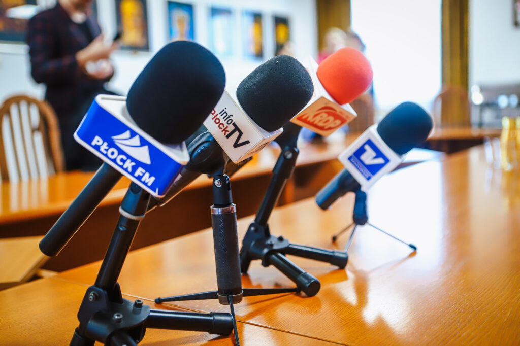 Zbliżenie na mikrofony z logotypami lokalnych mediów ustawione na stole podczas noworocznego śniadania prasowego samorządowców Powiatu Płockiego.
