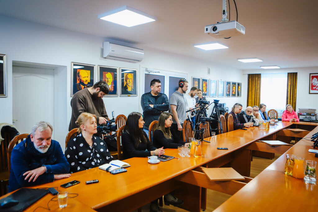 Grupa samorządowców i przedstawicieli lokalnych mediów siedzi przy długim stole w sali konferencyjnej podczas noworocznego śniadania prasowego Powiatu Płockiego.